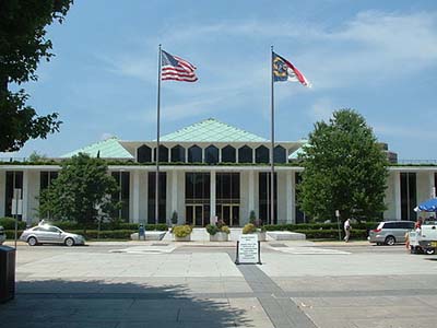 Un gran edificio blanco con muchos ventanales del suelo al techo. La bandera de los Estados Unidos y Carolina del Norte está al frente.