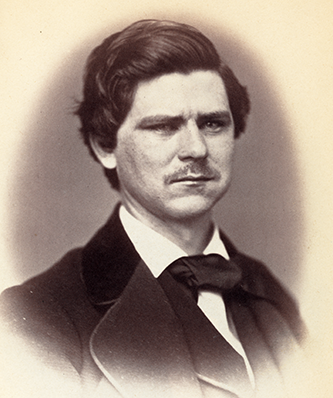Zebulon Baird Vance, a white man with medium length dark hair. He has a mustache and is wearing a dark coat, vest, white button up shirt, and dark neckcloth. He has a serious expression.