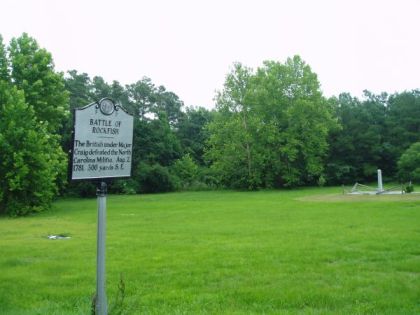 A large metallic marker in front of field circled by trees.  Marker reads: "BATTLE OF ROCKFISH, The British under Major Craig defeated the North Carolina Militia, Aug. 2, 1781, 300 yards S.E."
