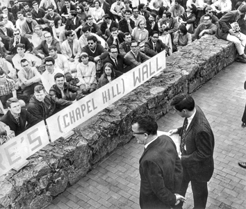 Banned speaker Frank Wilkinson (left) is introduced by student body president Paul Dickson from a public sidewalk on Franklin Street as students seated on the UNC campus listen.