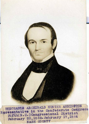 Arrington. He is wearing a suit and shirt with a black collar. He has short, styled hair, and is smiling.