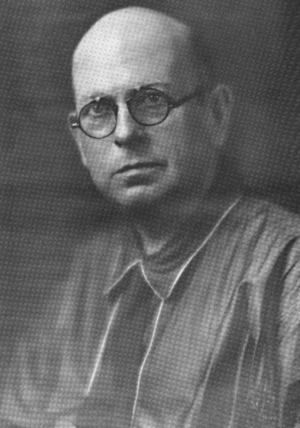 Saunders pictured. He is bald, and is wearing a collared shirt and glasses. He has a stern expression. 