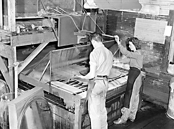 A man and woman operate a glass cutter in a furniture factory. 