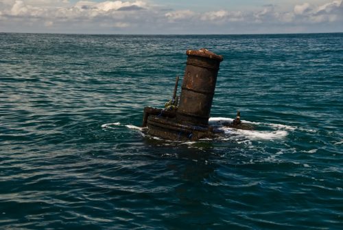 Rusted smokestack from a sunken steamer ship sticking out of the ocean with currents forming around it. 