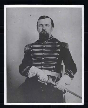 Posed portrait of William L. Saunders as a young man, wearing military dress, date unknown. The young man has a beard and mustache and is holding his sword, near his lap, with both hands.