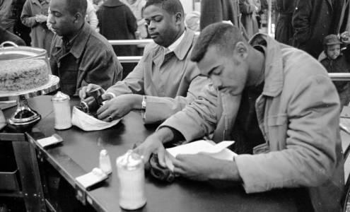 Three men sit at a bar. They are wearing nice clothes and they look frustrated and they are studying their books. They are black and have short hair. 