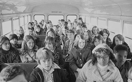 This is a photograph of two African American children and more than thirty white children riding in a school bus from the suburbs to an inner city school, Charlotte, North Carolina (1973).