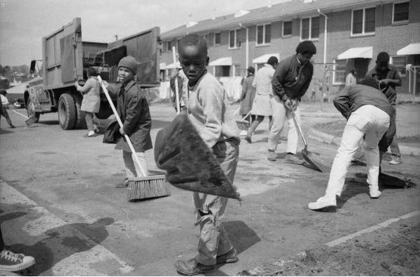 Photograph of men, women, and children using shovels and brooms to sweep a street during a clean-up campaign at McDougal Terrace in Durham, North Carolina, March, 1968.