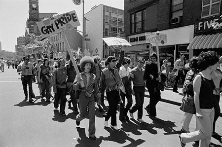 Men and women carry Gay Pride signs as they march through the streets of a city.
