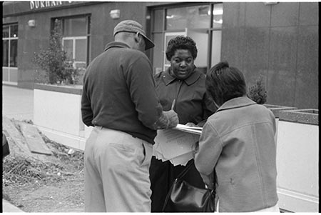 Photograph of Ann Atwater as she registers voters in Durham, N.C. Two individuals stand with her in the picture. They stand in front of a building in Durham.