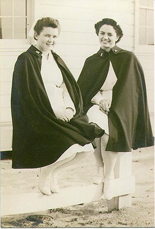 Snapshot of U.S. Army nurse Almyra M. Watson (left) and an unidentified nurse, wearing their Army Nurse Corps uniform and capes, sitting outside on a wooden fence on a beach next to a building at an unidentified military installation during World War II (from the John L. Watson Papers, WWII Papers, Military Collection, State Archives of North Carolina, Raleigh, N.C.).