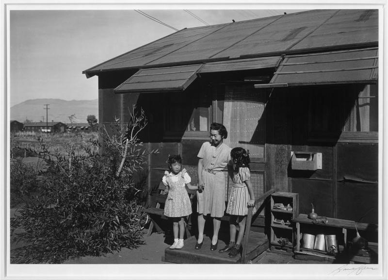 An Asian woman stands in front of her relocation house with her two daughters.