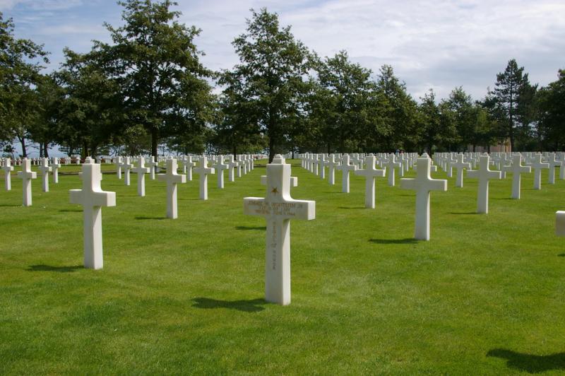 A graveyard. It is full of ceramic crosses. The grass is green and there are trees in the background. It is a sunny day. 