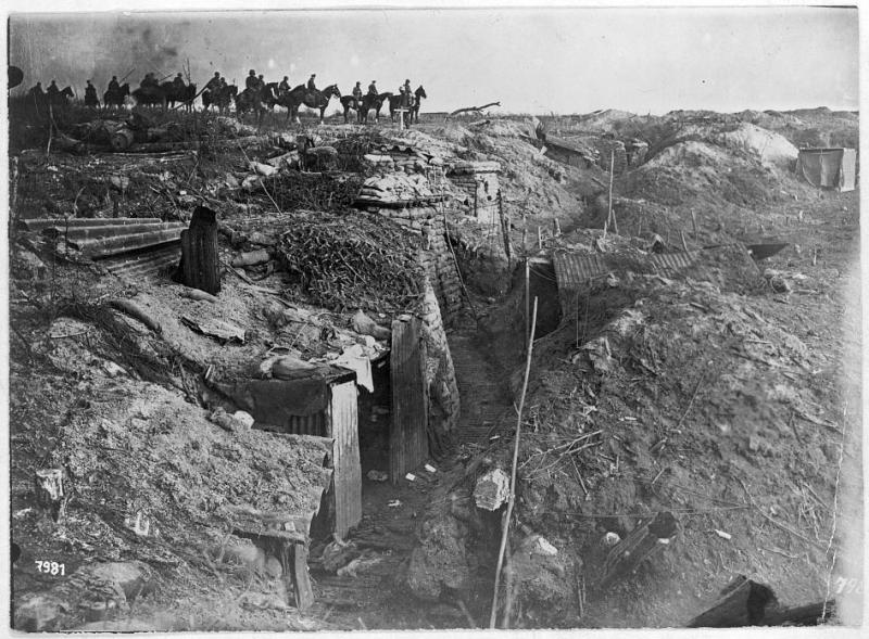 Horsemen sit on a ridge overlooking an abandoned defensive trench. Black and white photo.