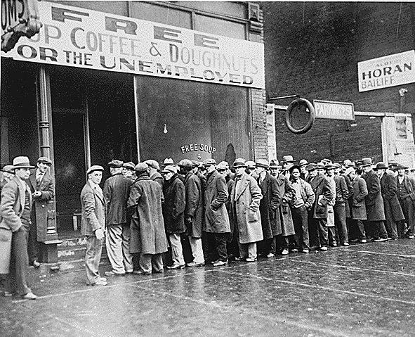 On a sidewalk, a line of people wait to be served. They are wearing winter apparel.