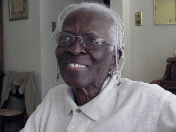 Louella Odessa Saunders Amar. She is an older woman. She has braids and glasses. She is smiling.