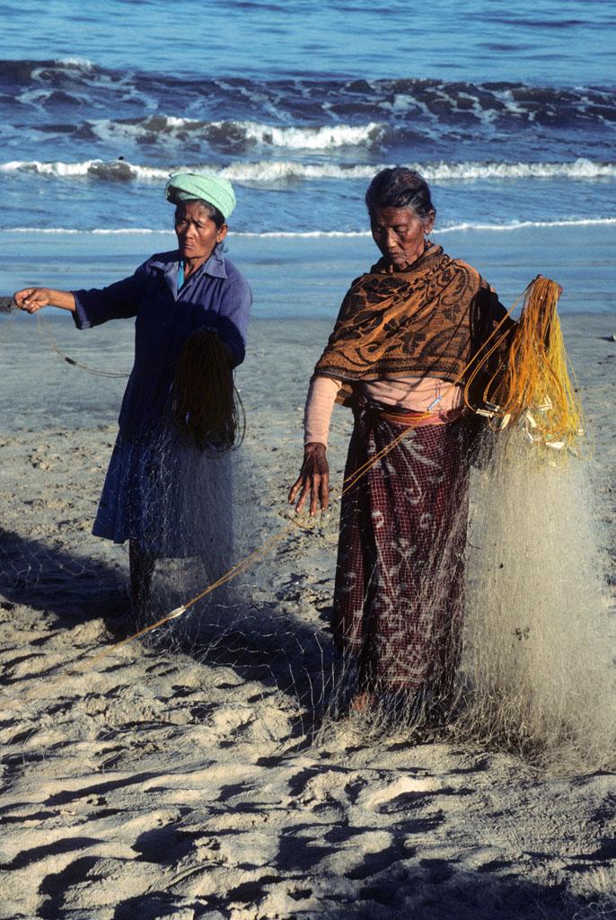 Two women fold large nylon fishing nets