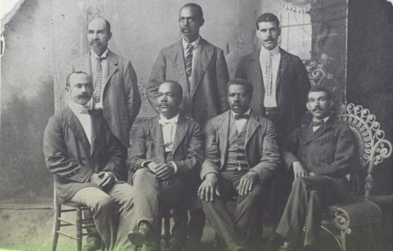 Six men in suits pose for a photo. Black and white photo.