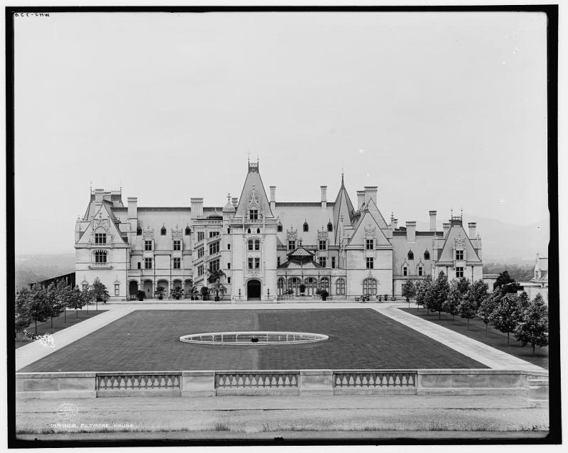 A photograph of Biltmore Estate, 1902. It is Gothic revival style and overlooks a large grassy area and a mountainside.