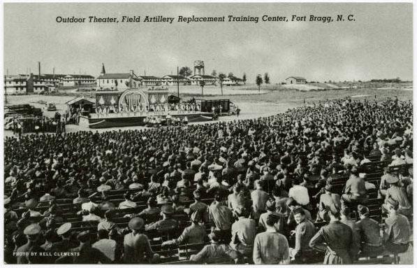 A postcard depicts hundreds of soldiers sitting in amphitheater. 