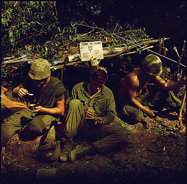 American soldiers in Vietnam sit in front of a fighting bunker bearing the handwritten sign “Home is where you dig it.”