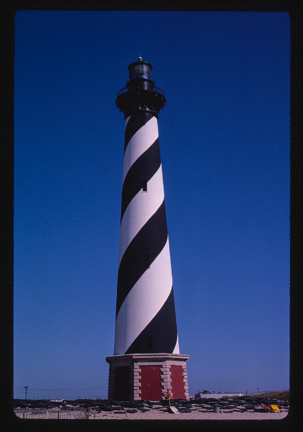 A photo of Cape Hatteras at its original location. The soil is sandy and the sky is blue. 