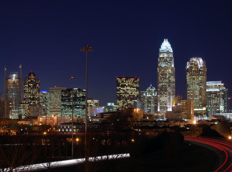 A nighttime skyline of the city of Charlotte, NC. There are several skyscrapers that are illuminated.
