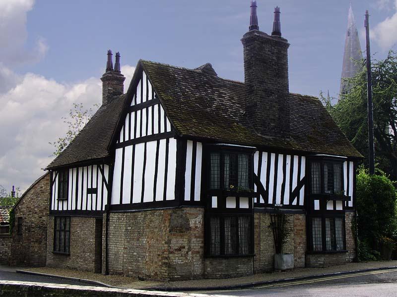 16th century Tudor style home. It is brick on the bottom half and wood on top. It is trimmed in dark woods and the sky is blue.