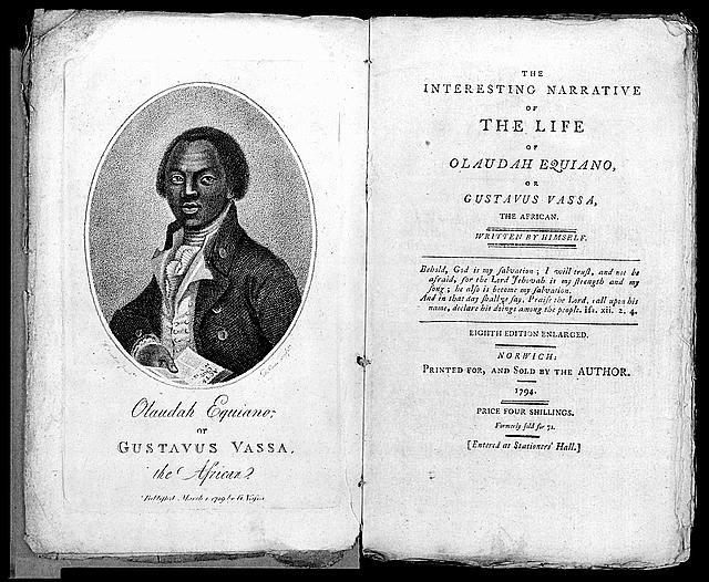 Olaudah Equiano. He is wearing a scarf, vest and jacket. His hair is parted. He is holding a book with a serious expression. He is young.