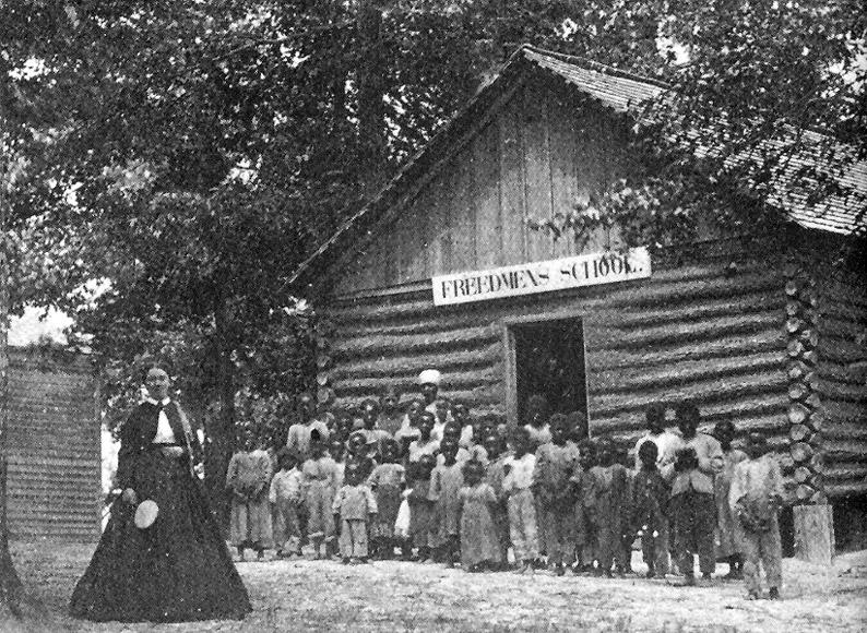 Students standing outside a freedmen's school. Trees are in the background.