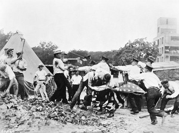 Bonus army members clash with police. They fight on rubble near makeshift tents.