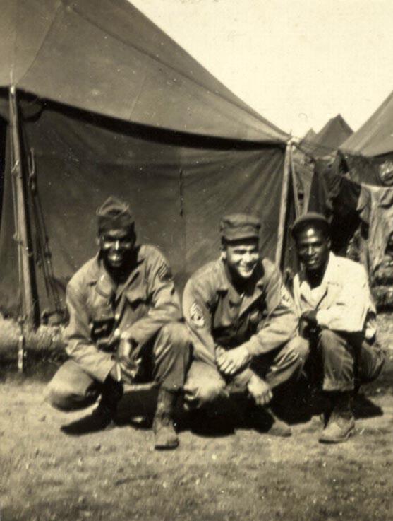 This is a black and white print of soldiers crouching with tents in the background, Fort Francis E. Warren, Wyoming, 1943. Soldiers from left to right are "unidentified," First Sergeant Southall, and Staff Sergeant Odra W. Bradley.