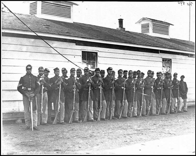 27 African Americans of Company E during the Civil War, standing in two lines with rifles resting on the ground.