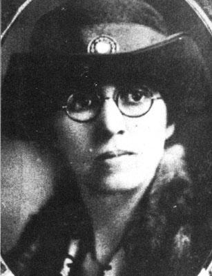 Lilian Exum Clement. She is facing the camera. She is wearing glasses and a fancy hat with a jewel on the front of it. Her lips are pursed. Black and white. 