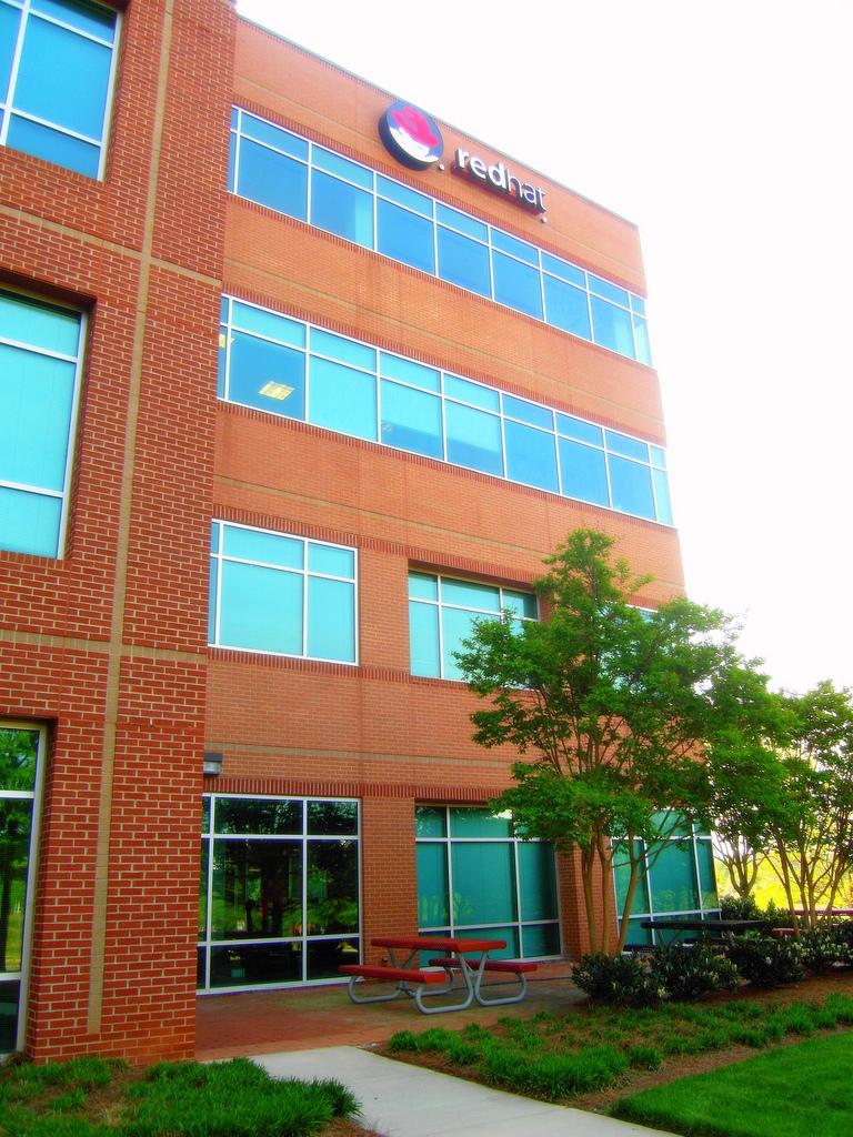 RedHat building. It is a sunny day and there are plants in front. There is a paved sidewalk. 