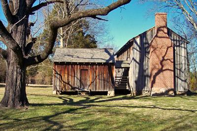 Stagville Plantation. Two wooden buildings with a large tree in front. It is a sunny day with blue skies.