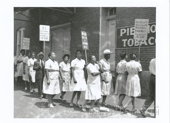 People, mostly women in dresses, strike in front of a brick building