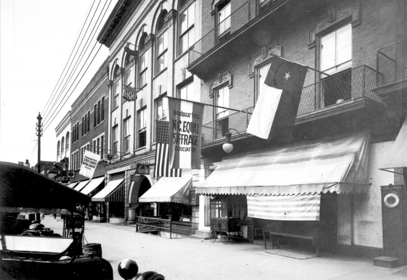 A building with a flags hanging outside, one of which reads "North Carolina Equal Suffrage Association." 