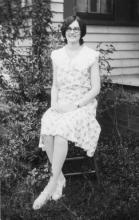 black and white image of a dark-haired young lady sitting on a chair outdoors
