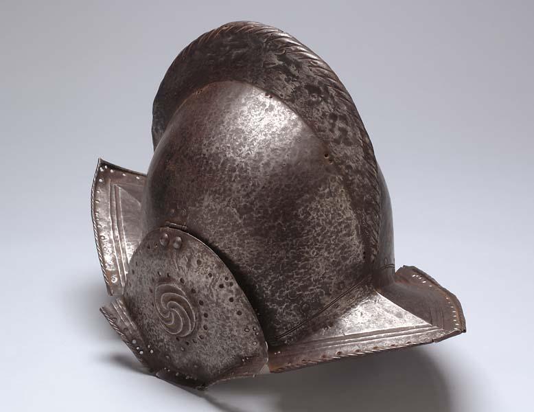 Metal helmet. It is pointed on both ends and has a smooth ridge that follows the length of the helmet. There are elevated sections where the ears would like go with a design on them. 