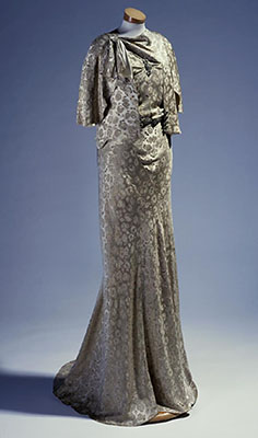 A floor-length, gold, patterned dress on a dress form.