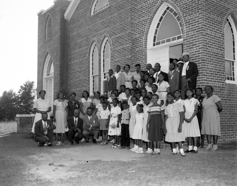 A group of Black people stand outside a brick church in Manteo