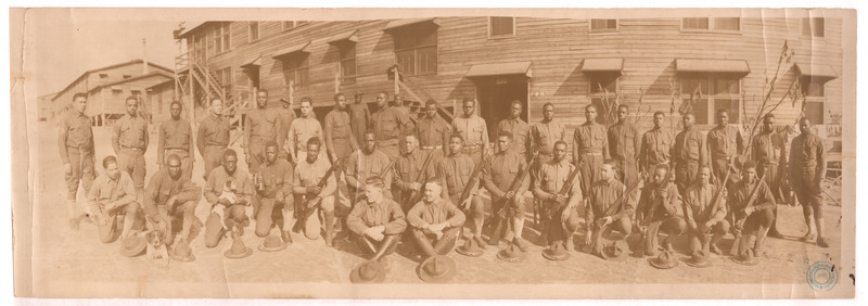 Black men in uniform two rows stand or kneel with rifles while two white men in uniform sit in front