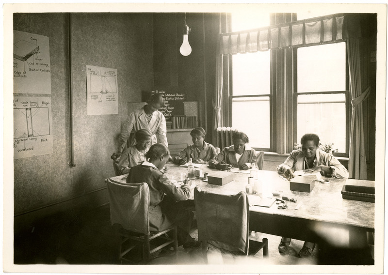 Six Black women sit around a table working to repair books