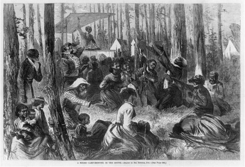 A camp meeting scene. The attendees are all black. An impassioned orator stands at a lectern, preaching to the crowd.