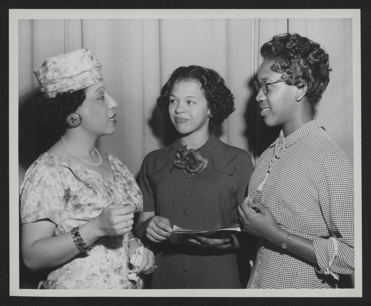 Elreta Alexander talking to two other women. She is pictured far left, appearing to be mid sentence. All women are dressed in nice clothes.