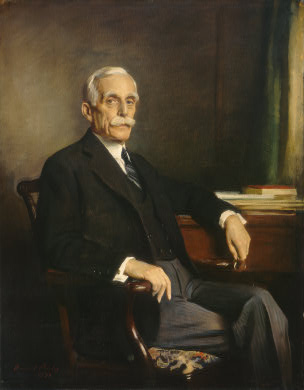 Andrew Mellon. He is sitting in a study. He is wearing a suit and has a thick moustache. 