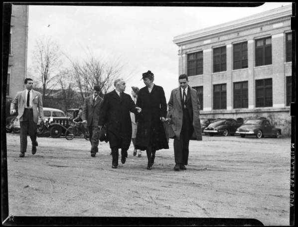 Eleanor Roosevelt walks with students on Chapel Hill's campus. They are all wearing trench coats. Black and white photo.