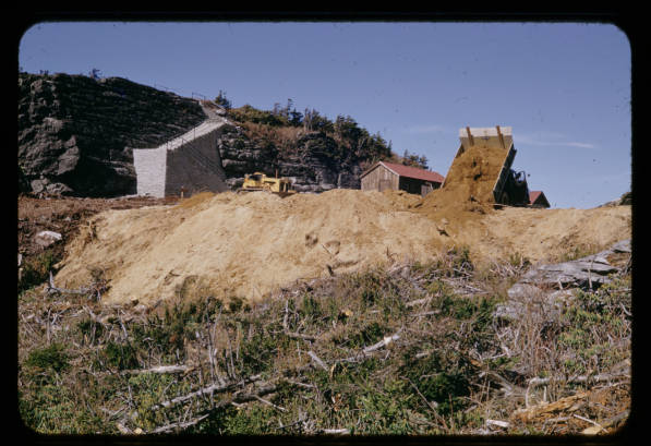 A dump truck lays sand and other foundation at a job site.