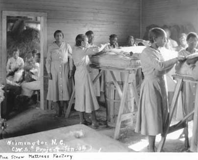 Women in a crowded wooden room stuff mattresses.